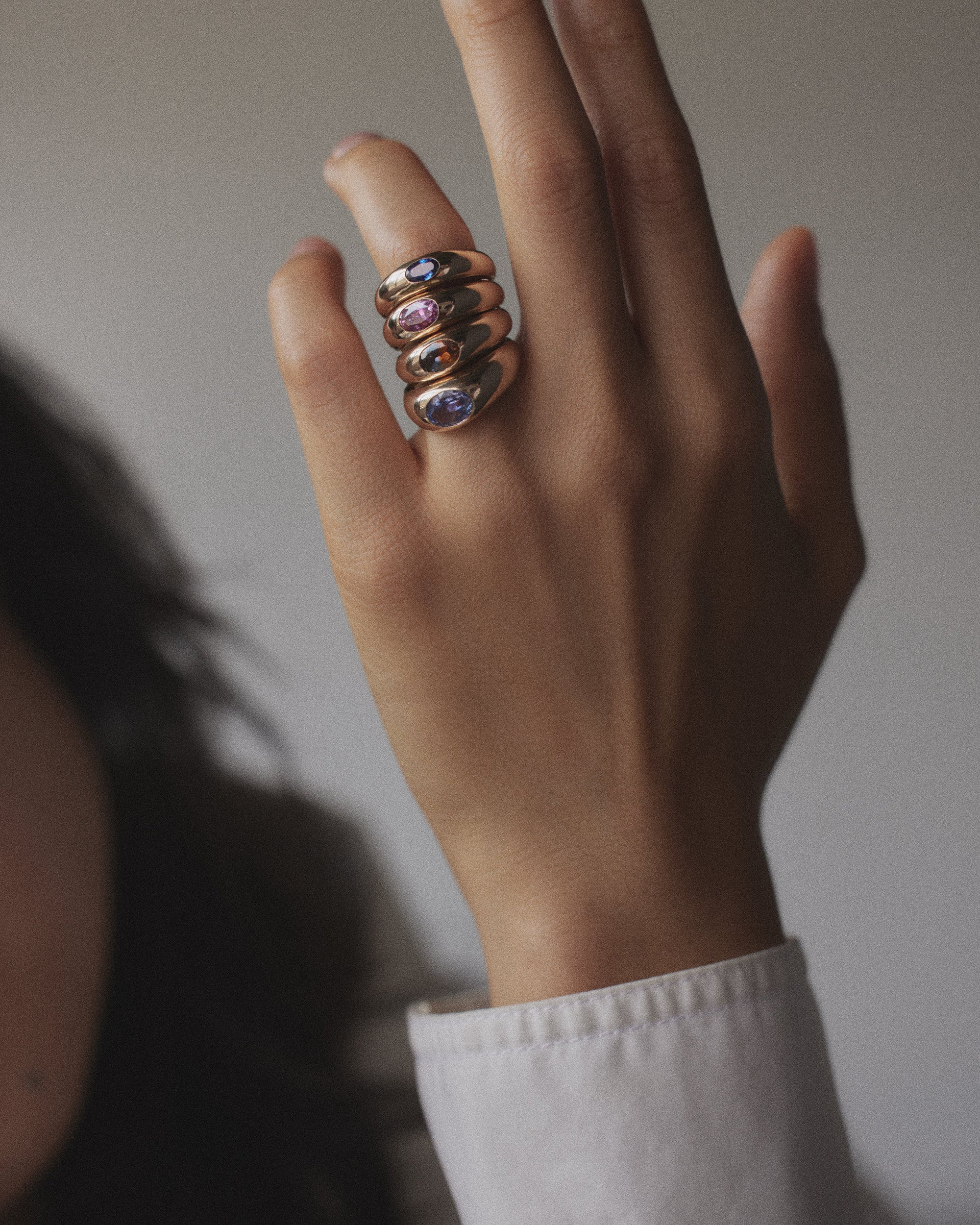 [lifestyle]Hand wearing multiple rings with gemstones on a neutral background