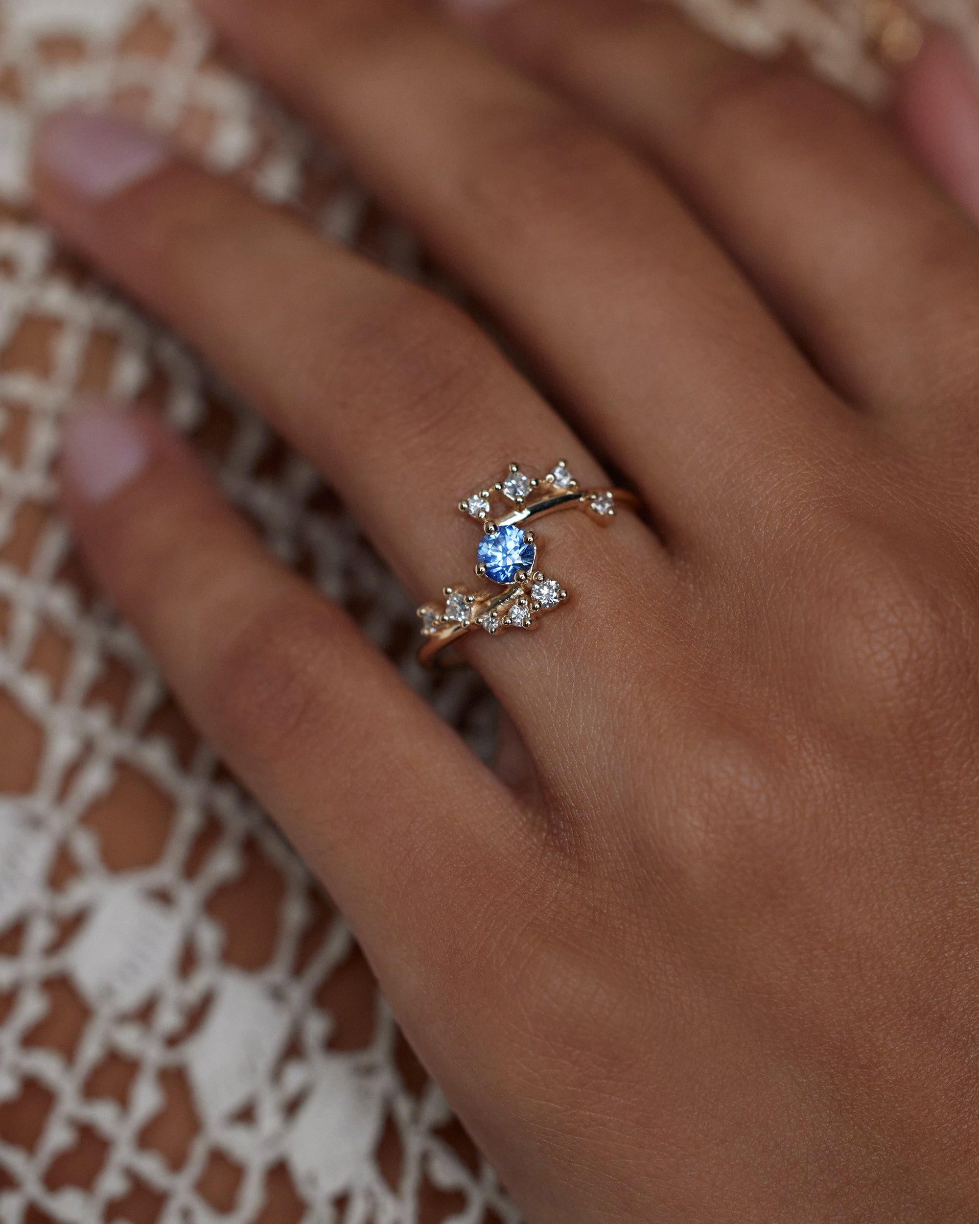 [lifestyle]Close-up of a hand wearing a ring with a blue gemstone on a textured fabric background
